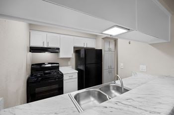 A kitchen with a black refrigerator, white oven, and a stainless steel sink.